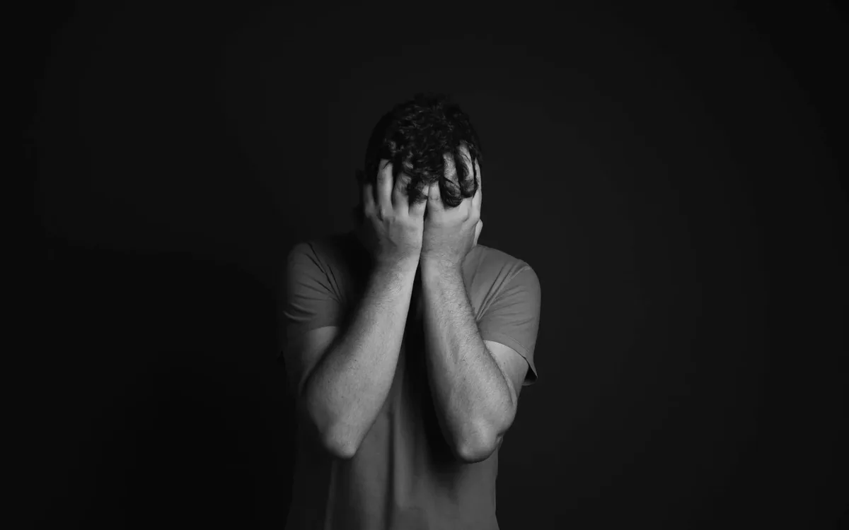 Homem cabisbaixo com as mãos no rosto, retrato em preto e branco